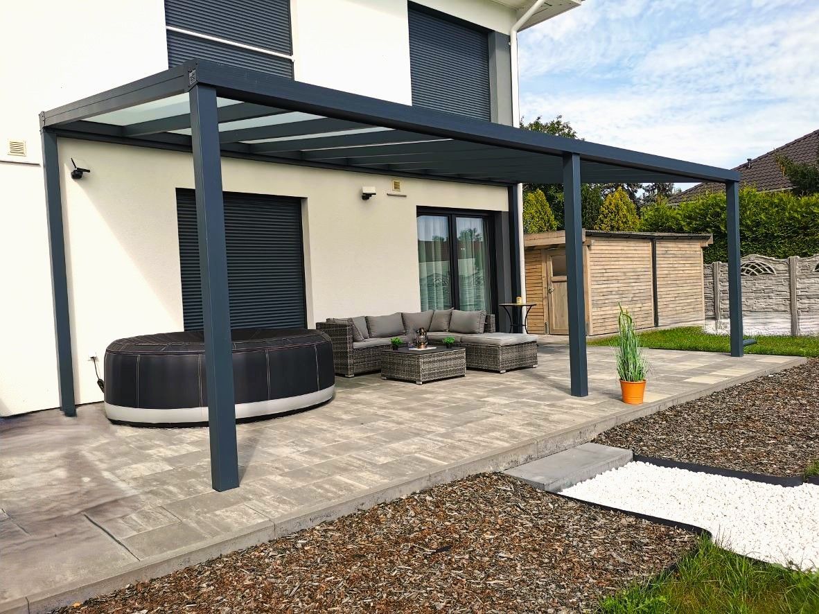 Eine Terrasse mit Pergola und Couch vor einem Haus.