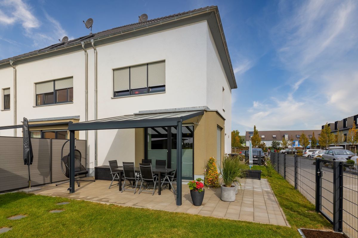Ein weißes Haus mit einer Terrasse und einer Pergola davor.