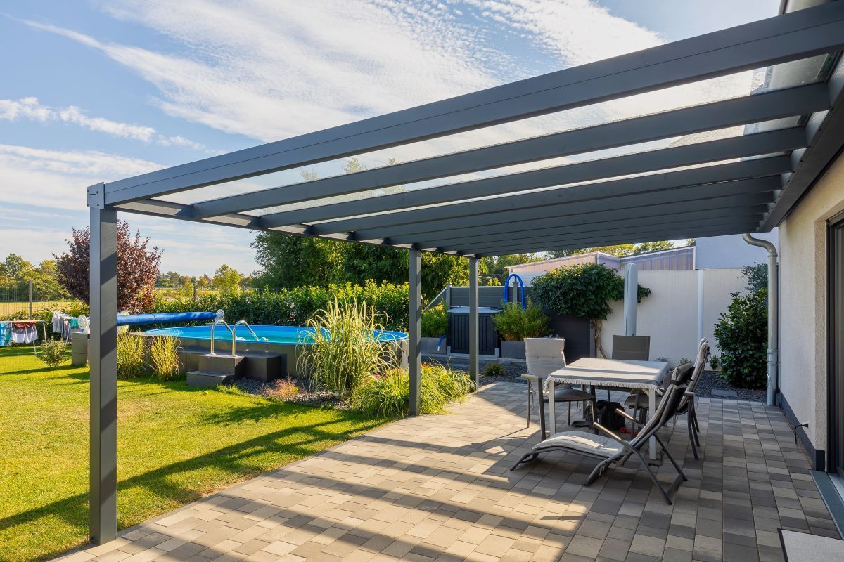 Eine Terrasse mit Tisch und Stühlen unter einer Pergola mit einem Pool im Hintergrund.