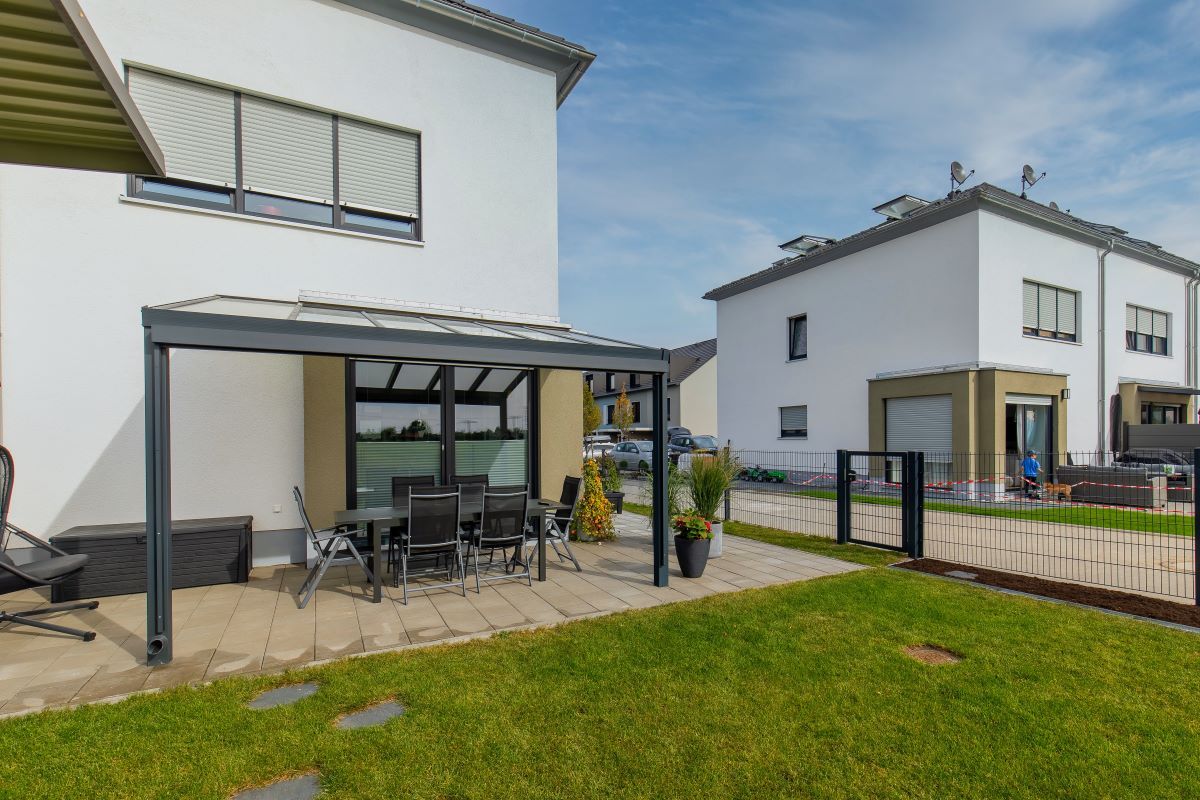 Eine Terrasse mit Tisch und Stühlen unter einer Pergola vor einem Haus.