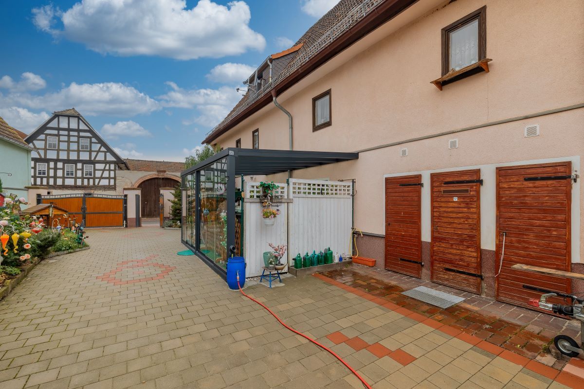 Ein Haus mit einer gepflasterten Auffahrt und einem Gewächshaus davor.