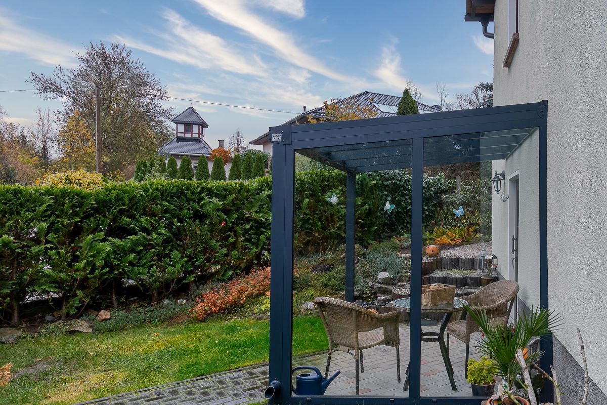 Eine Terrasse mit Tisch und Stühlen unter einer Pergola im Hinterhof eines Hauses.