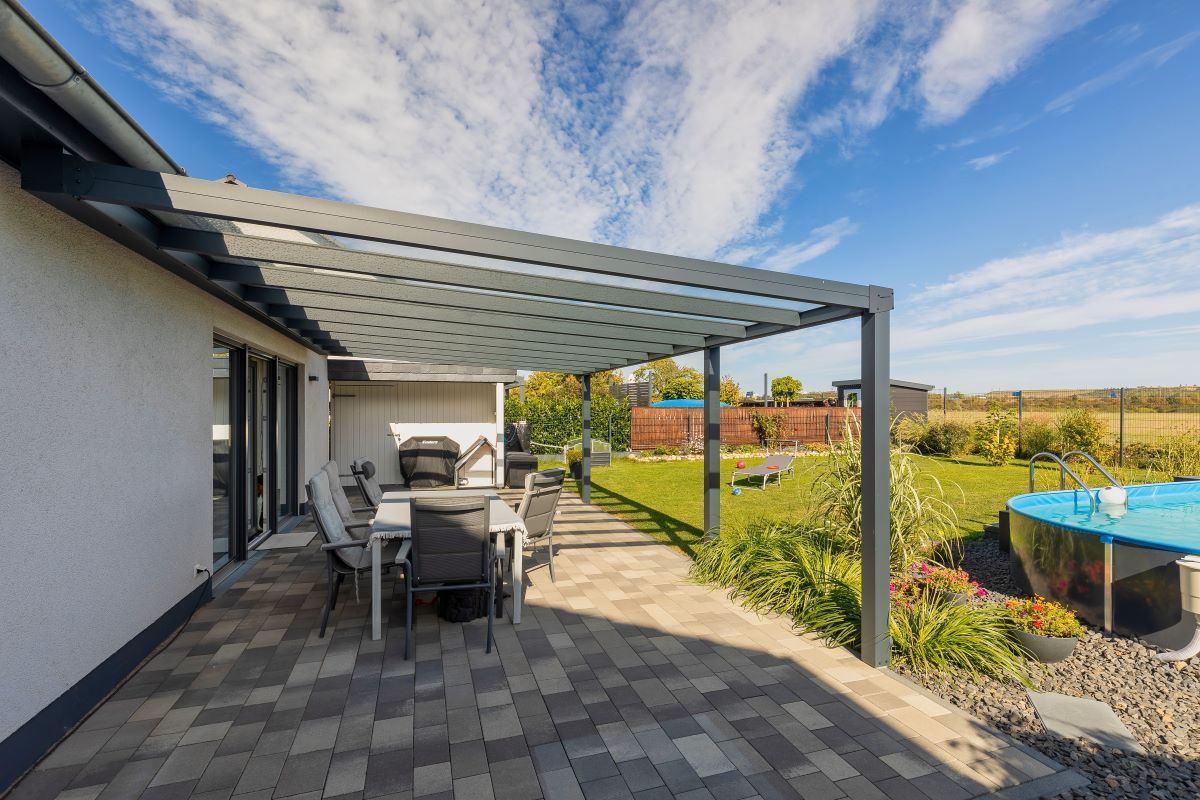 Eine Terrasse mit Tisch und Stühlen unter einer Pergola neben einem Pool.