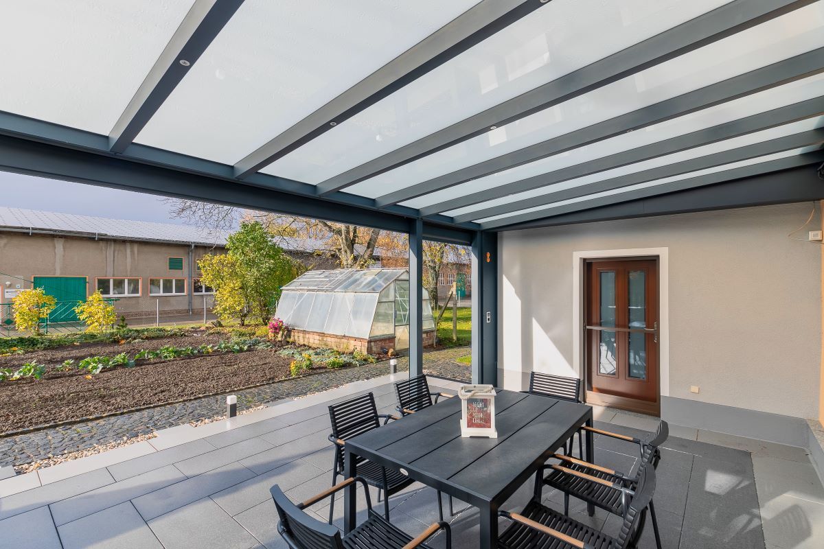 Eine Terrasse mit Tisch und Stühlen unter einem Glasdach.