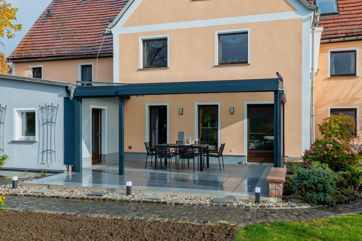 Ein großes Haus mit einer Terrasse mit Tisch und Stühlen unter einer Pergola.