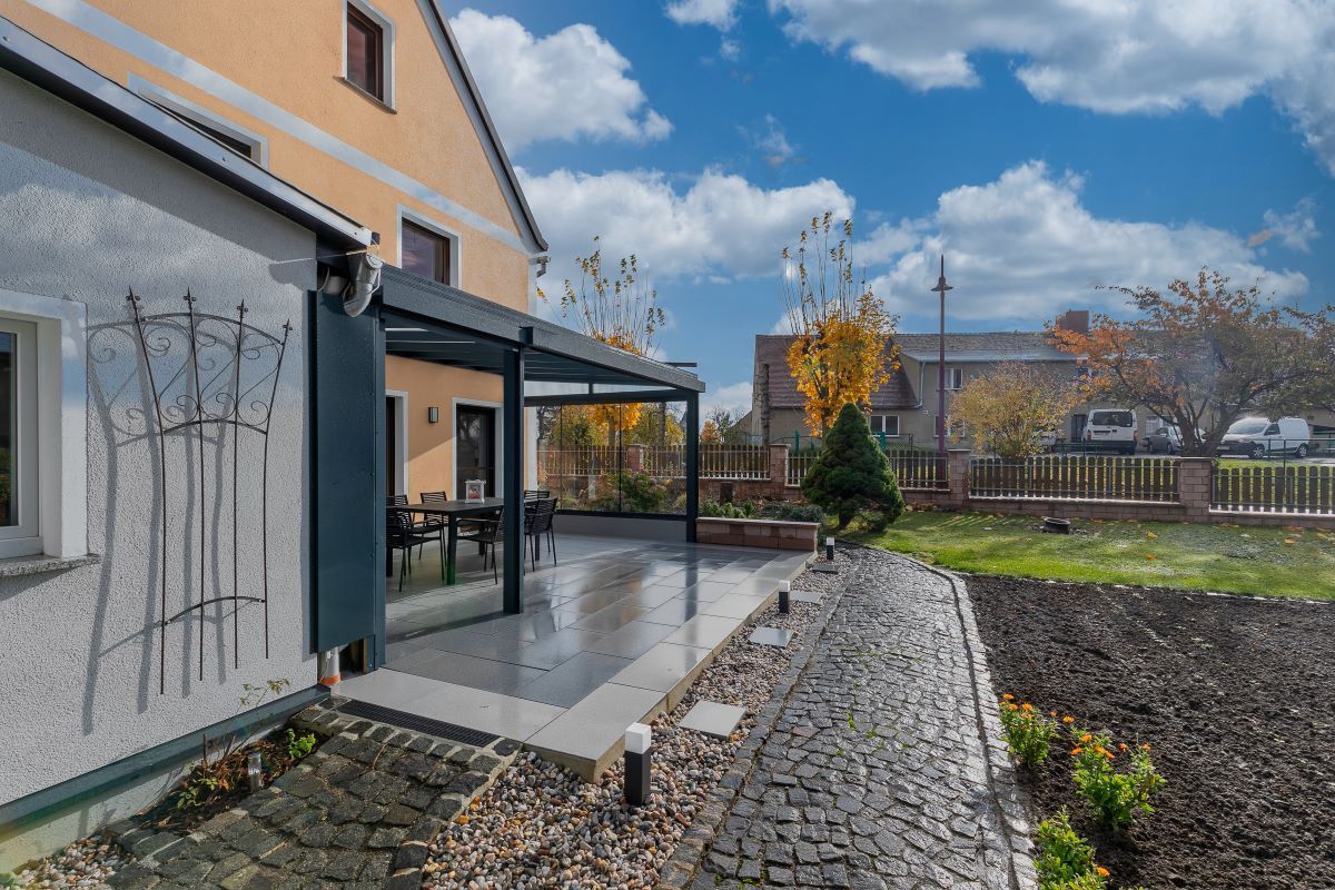 Ein Haus mit Terrasse und davor liegender Pergola.