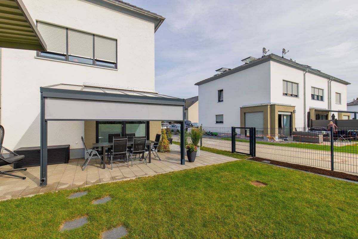 Ein Haus mit Terrasse und davor liegender Pergola.