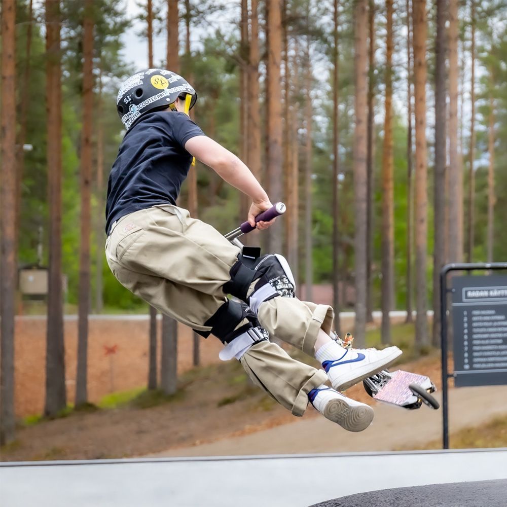 Poika potkulaudalla hyppimässä skeittipuistossa kypärä ja suojukset päässään.