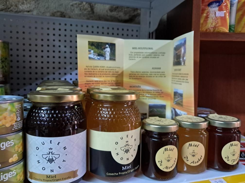 Frascos de miel y conservas en un estante de una tienda con un folleto de productos abierto detrás.