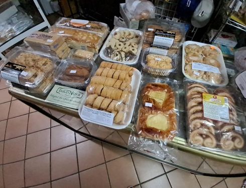 Exhibición de panadería con pasteles variados en bandejas de plástico transparente sobre un mostrador de azulejos.