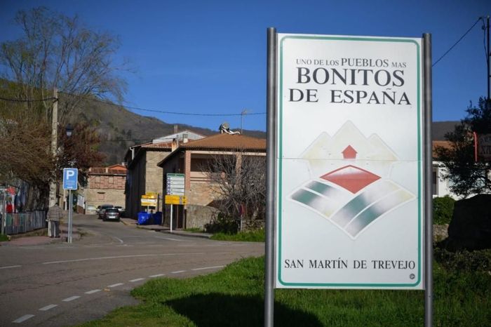 Roadside sign reading “Bonitos de España” in San Martín de Trevejo, beside a quiet street under a blue sky.