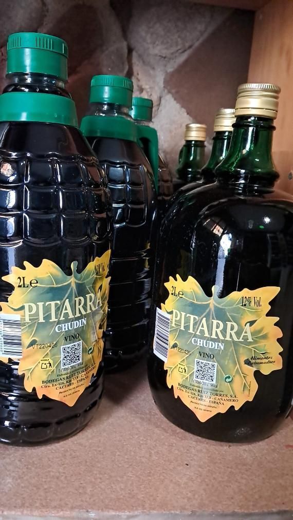 Dos botellas de aceite de oliva oscuro con tapones verdes y etiquetas doradas en un estante.