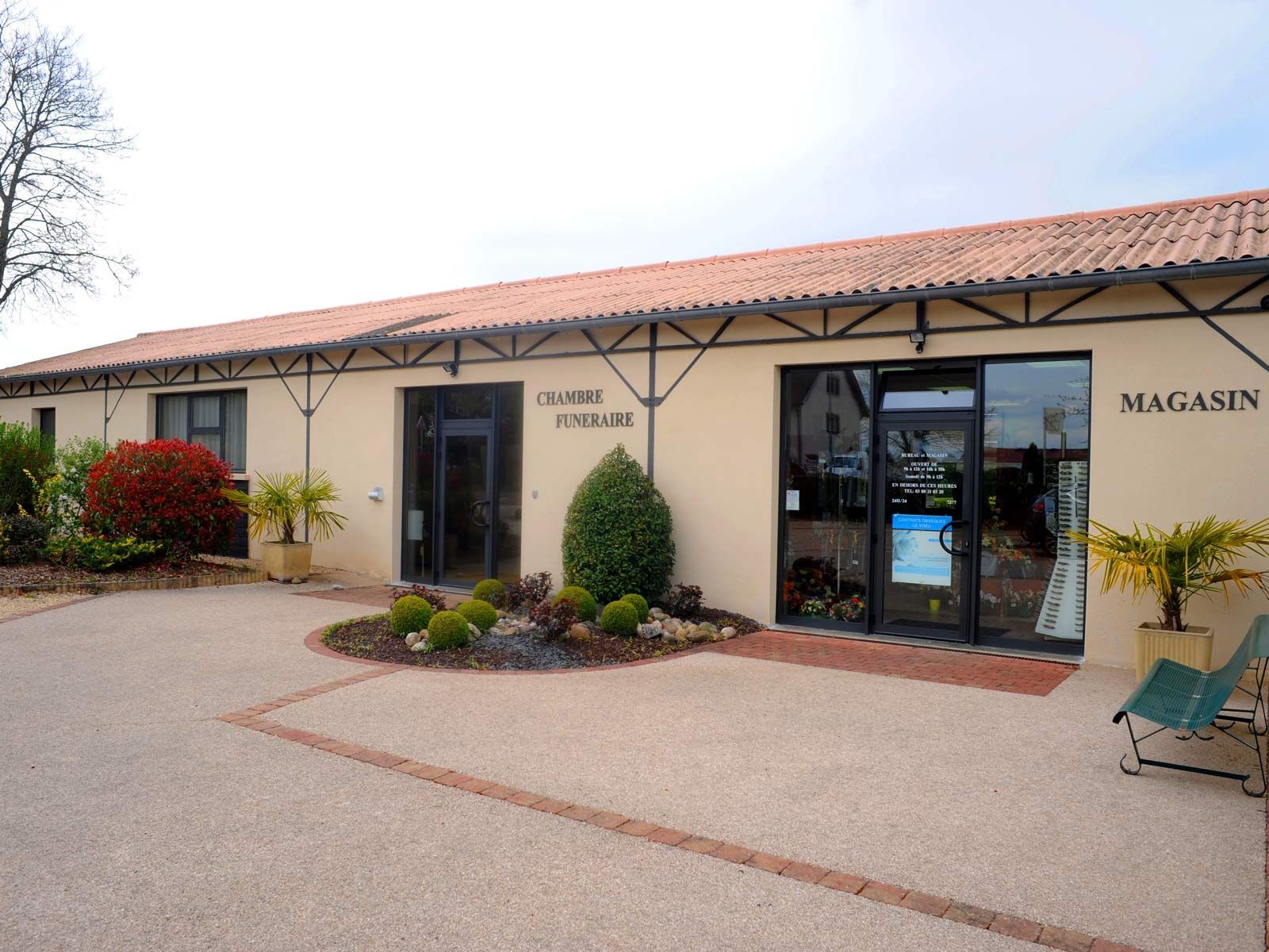 Extérieur d'une boutique beige au toit de tuiles rouges, portes vitrées et cour de gravier sous des arbres dénudés