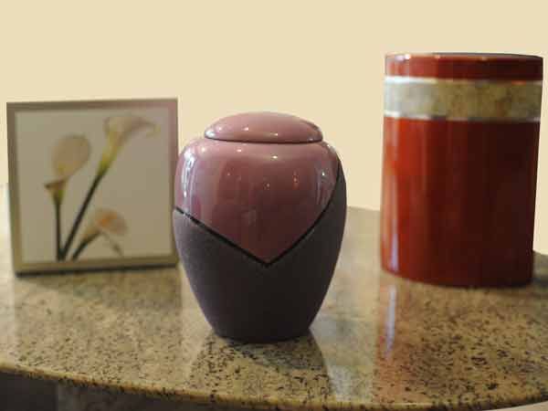 Trois bocaux décoratifs sur un comptoir, dont une urne à couvercle rose et violet au centre.