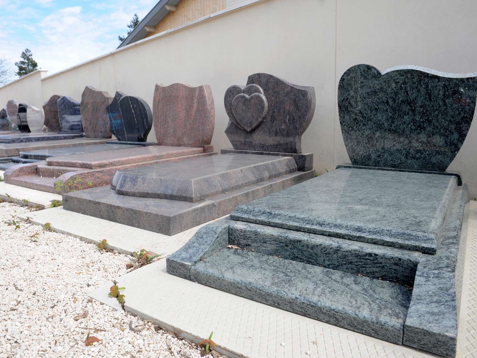 Rangée de pierres tombales en granit gravées dans un cimetière, dont une en forme de cœur, près d'un mur