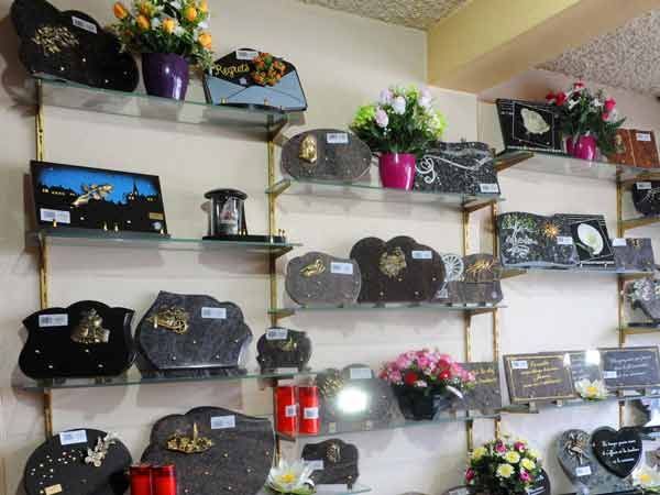 Des étagères remplies de plaques commémoratives et de compositions florales sont disposées sur un mur.