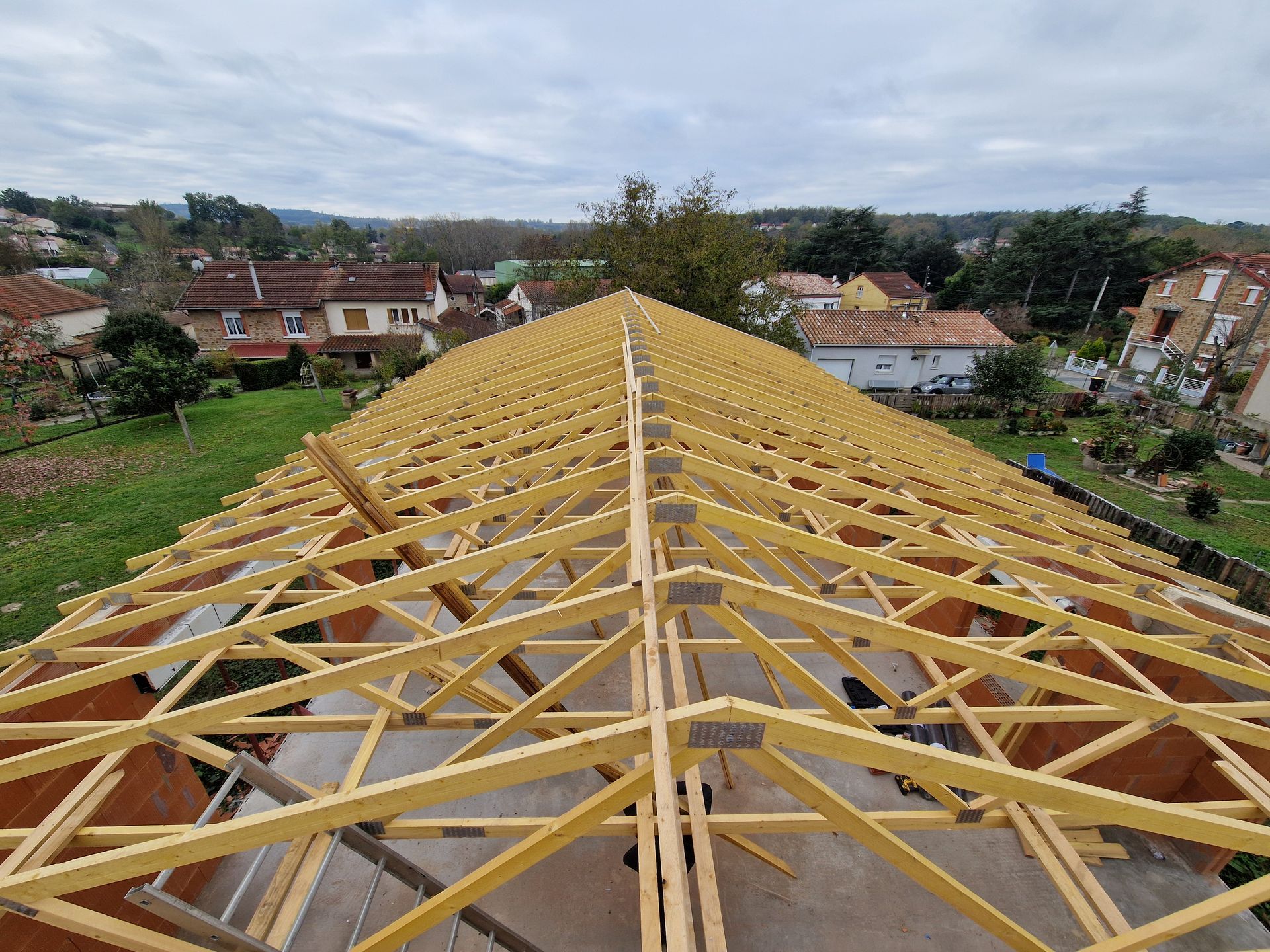 Un toit de tuiles en terre cuite sur un bâtiment en pierre, sous un ciel bleu, avec quelques arbres verts en arrière-plan.