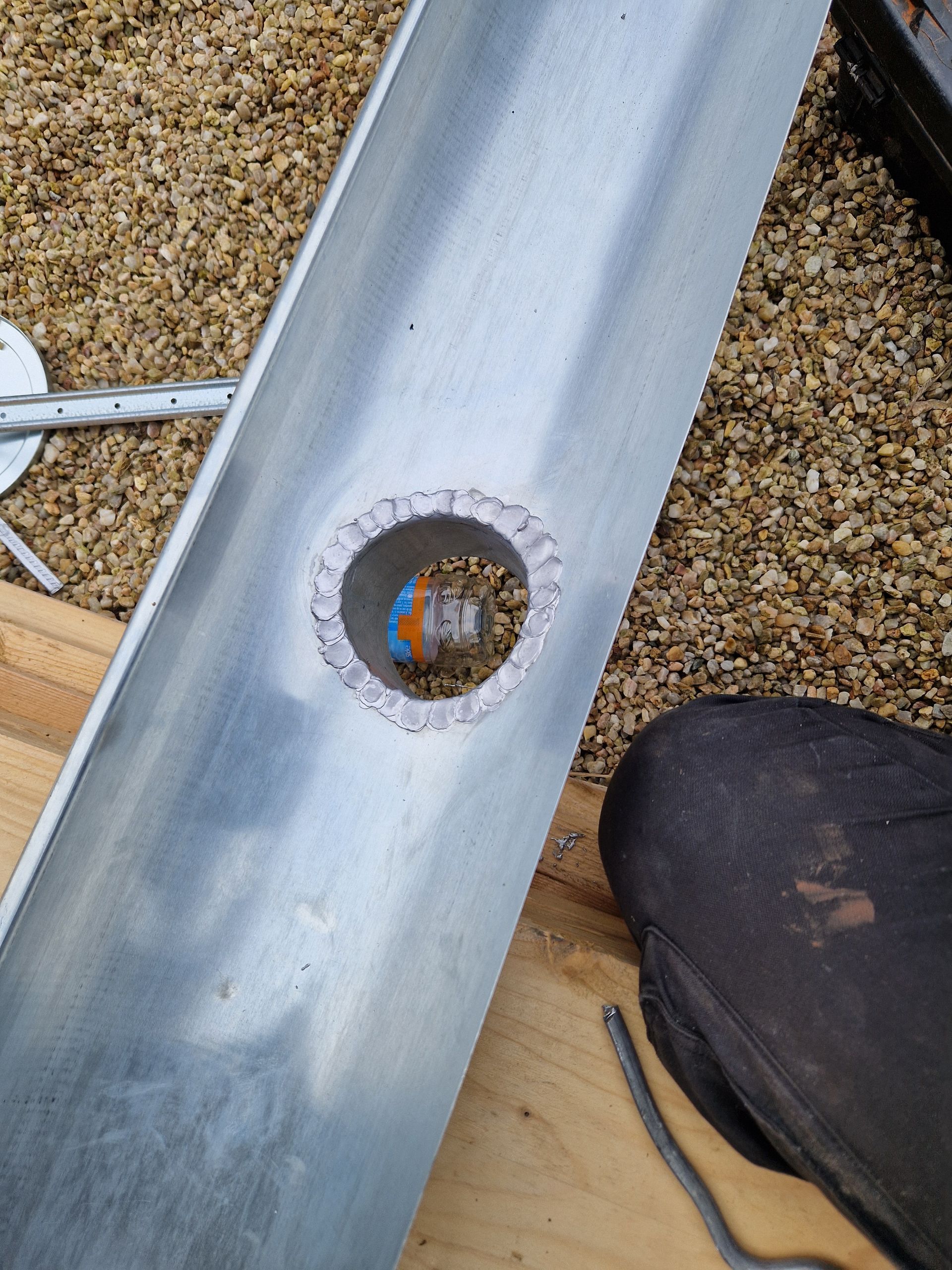 Cheminée avec solin métallique sur un toit de tuiles en construction, entourée d'outils.