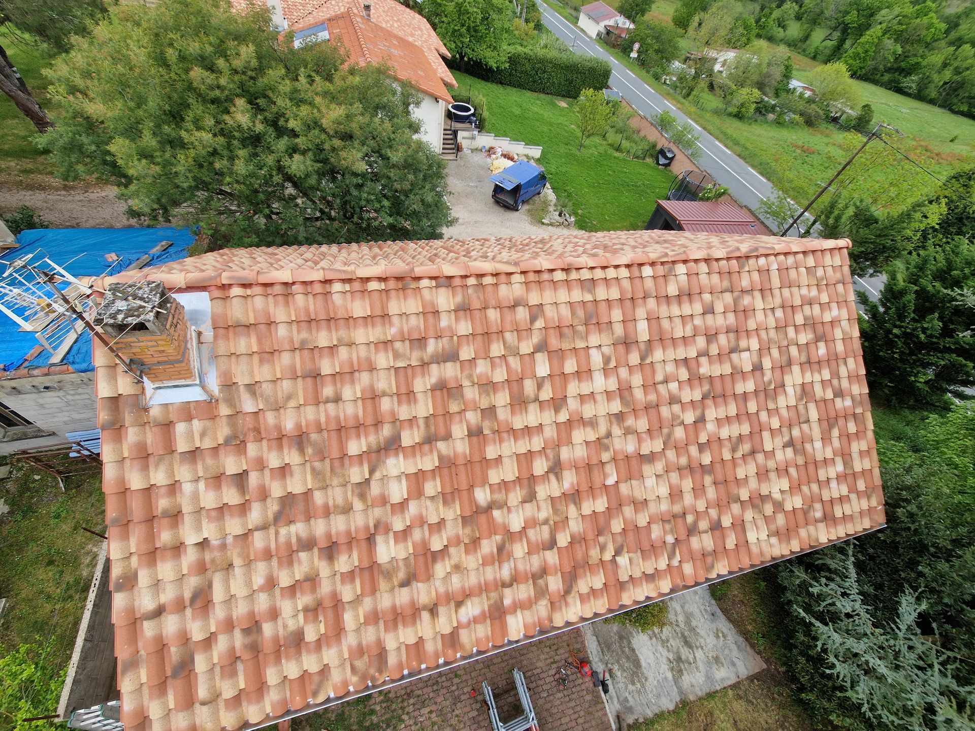 Toit de tuiles rouges avec une cheminée blanc et brun sur un ciel bleu.