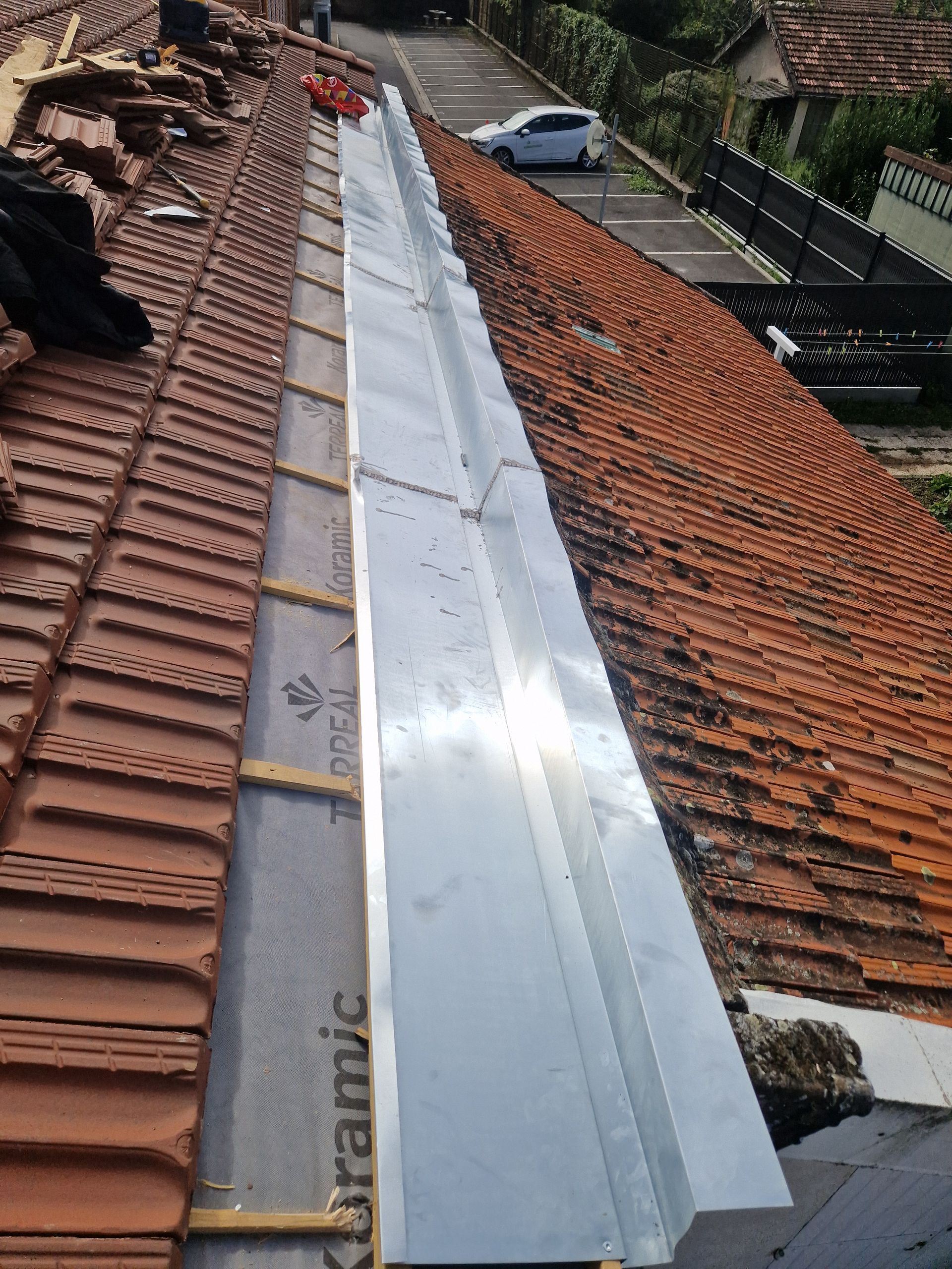 Toiture en tuiles de terre cuite avec une noue centrale en métal.