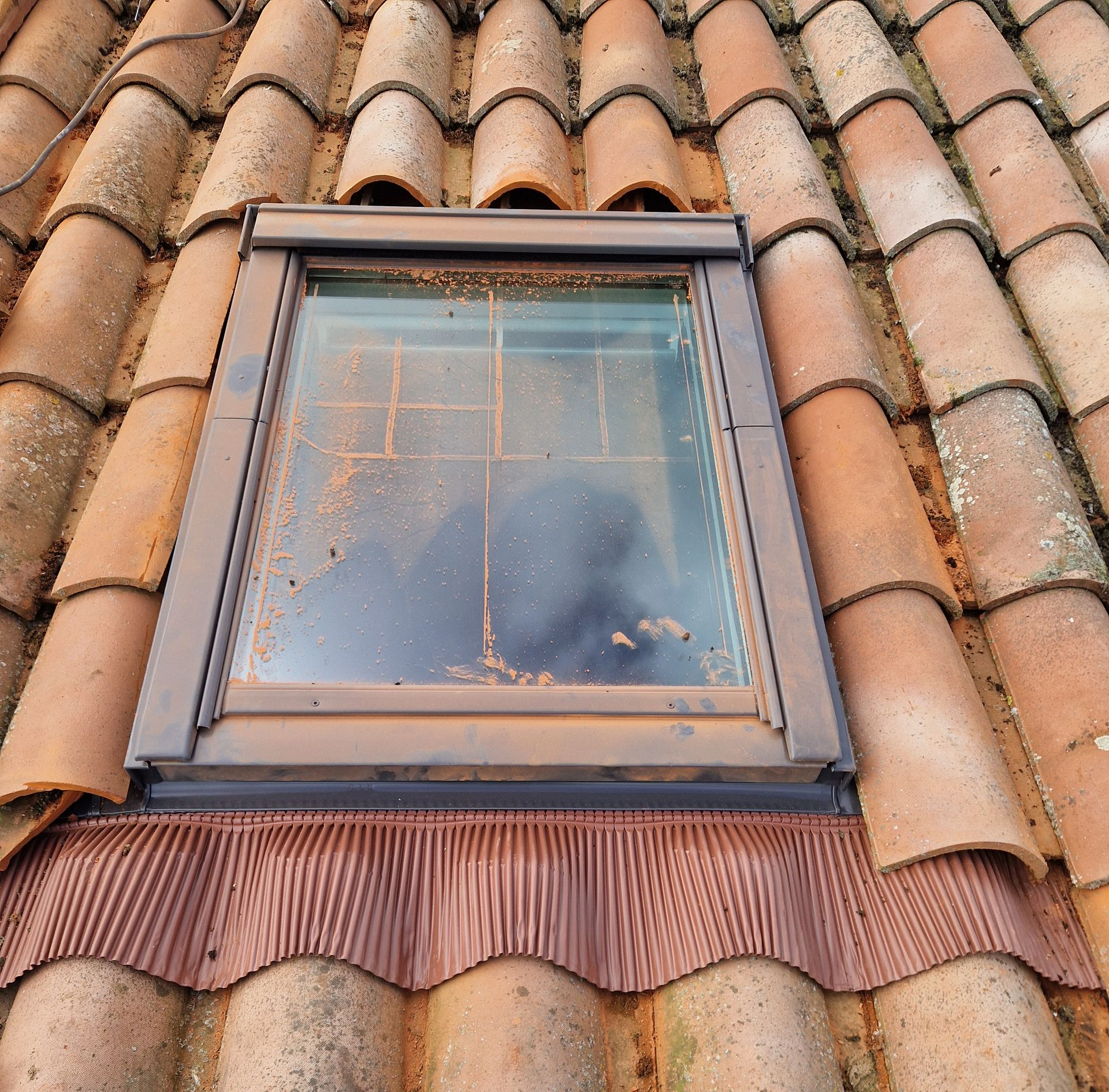 Toit de tuiles en terre cuite d'un bâtiment aux murs de pierre, sous un ciel d'un bleu limpide.