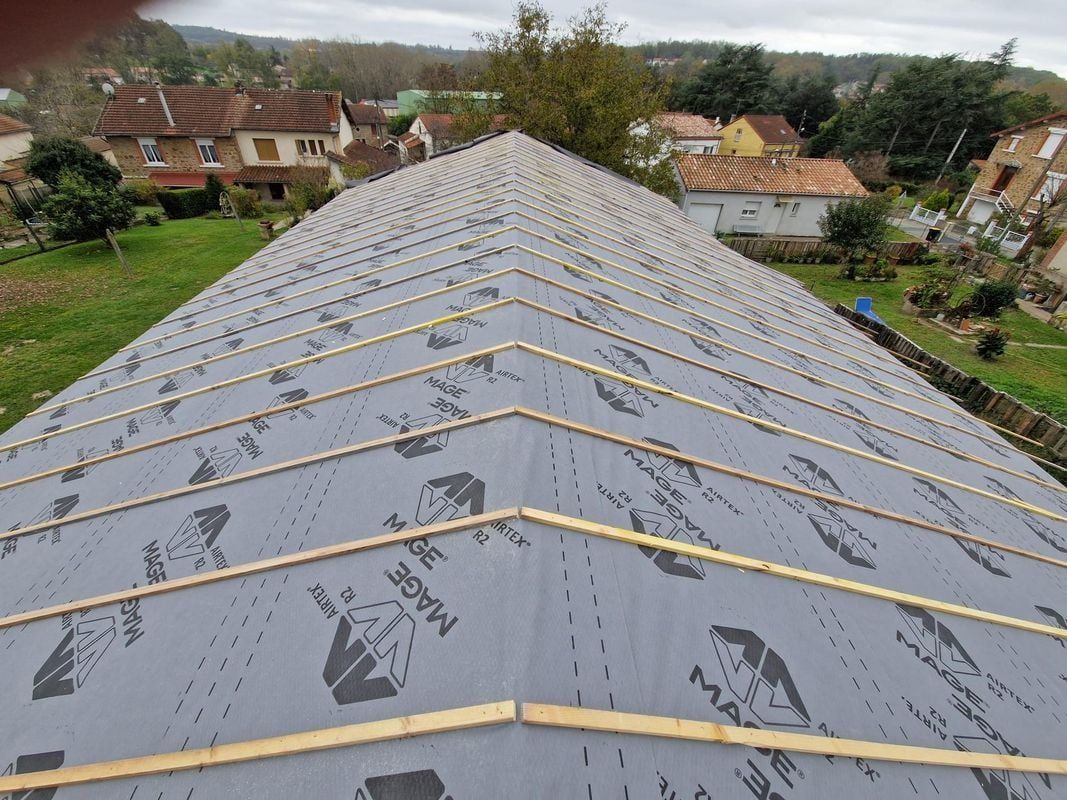 Vue aérienne d'un toit en construction ; sous-couche grise avec poutres en bois posées, arrière-plan de maisons et d'arbres.