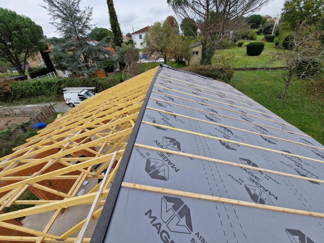 Construction d'un toit. Un côté est constitué de poutres en bois, l'autre de matériaux de couverture gris foncé et de supports en bois. Extérieur.