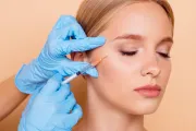 Manos enguantadas ajustando un hilo cerca del ojo de una mujer durante un procedimiento cosmético.