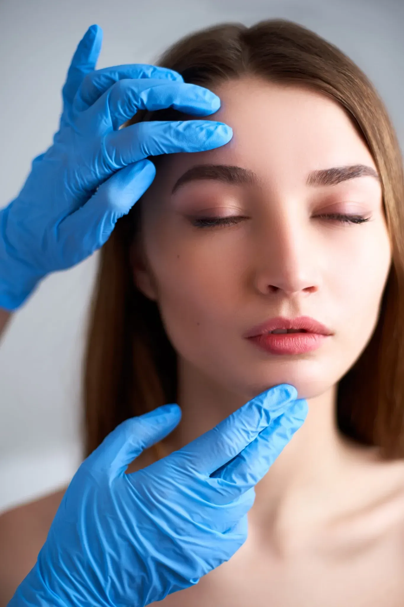 Manos enguantadas examinan con delicadeza el rostro de una mujer en una escena de tratamiento de belleza en primer plano.