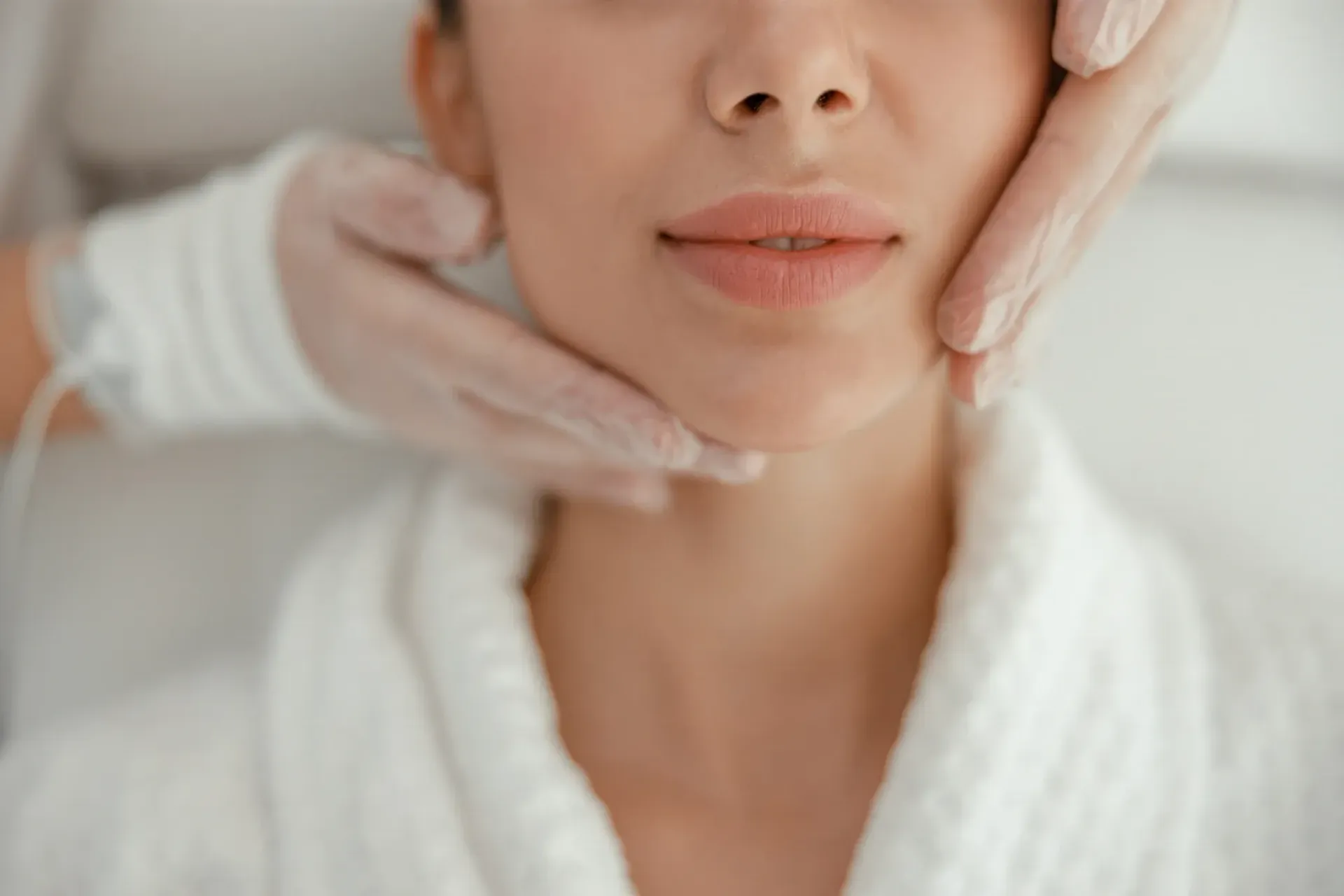 Primer plano de una persona con una bata blanca que está recibiendo un tratamiento facial.
