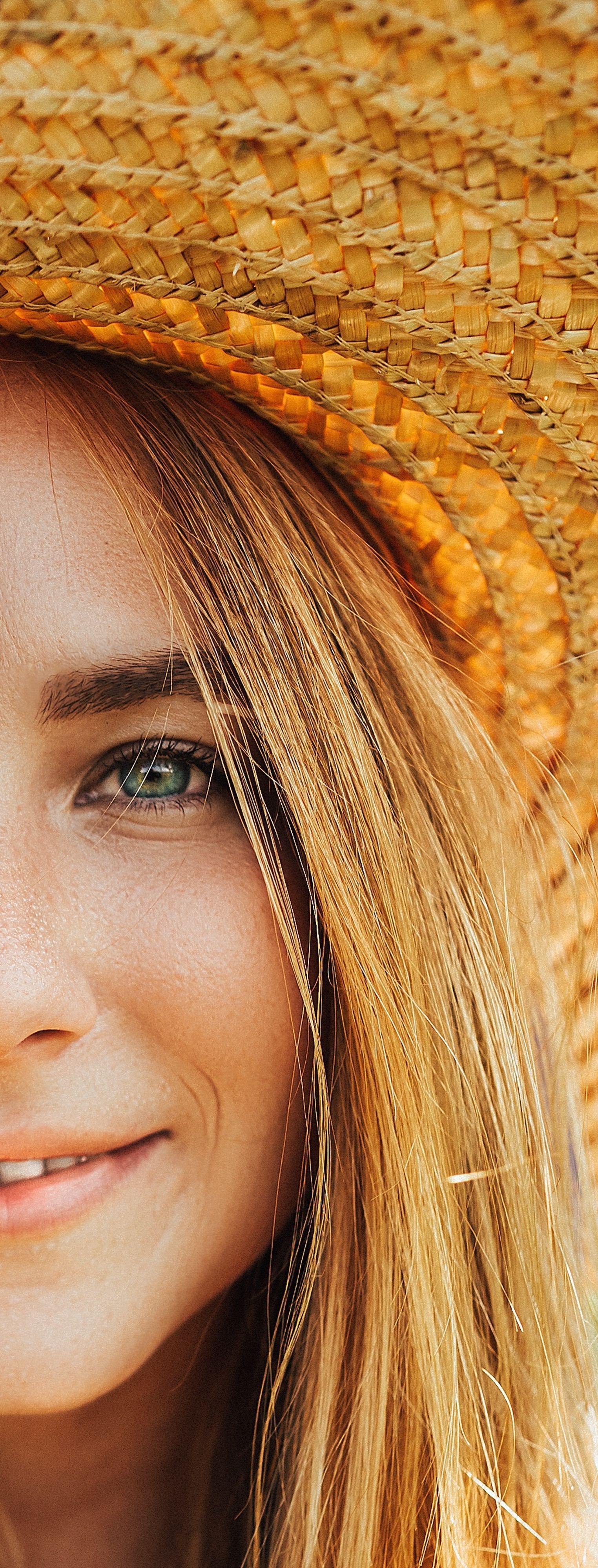 Primer plano de una persona sonriente con un sombrero de paja y cabello rubio iluminado por el sol.