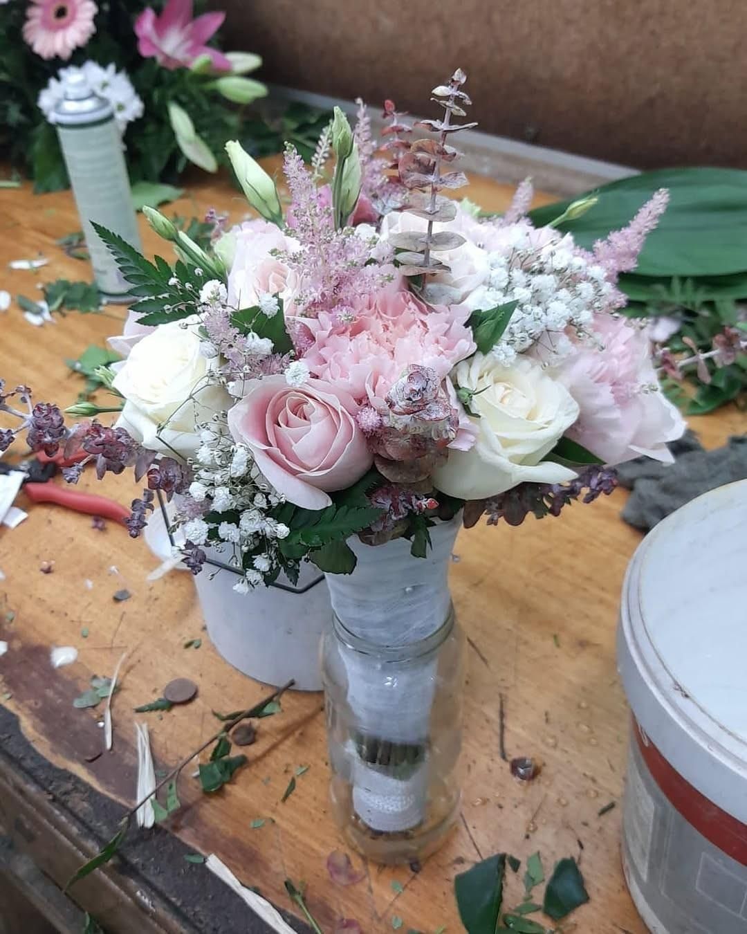 Un ramo de novia compuesto de rosas rosas y blancas, astilbe y paniculata, sostenido en un frasco de vidrio
