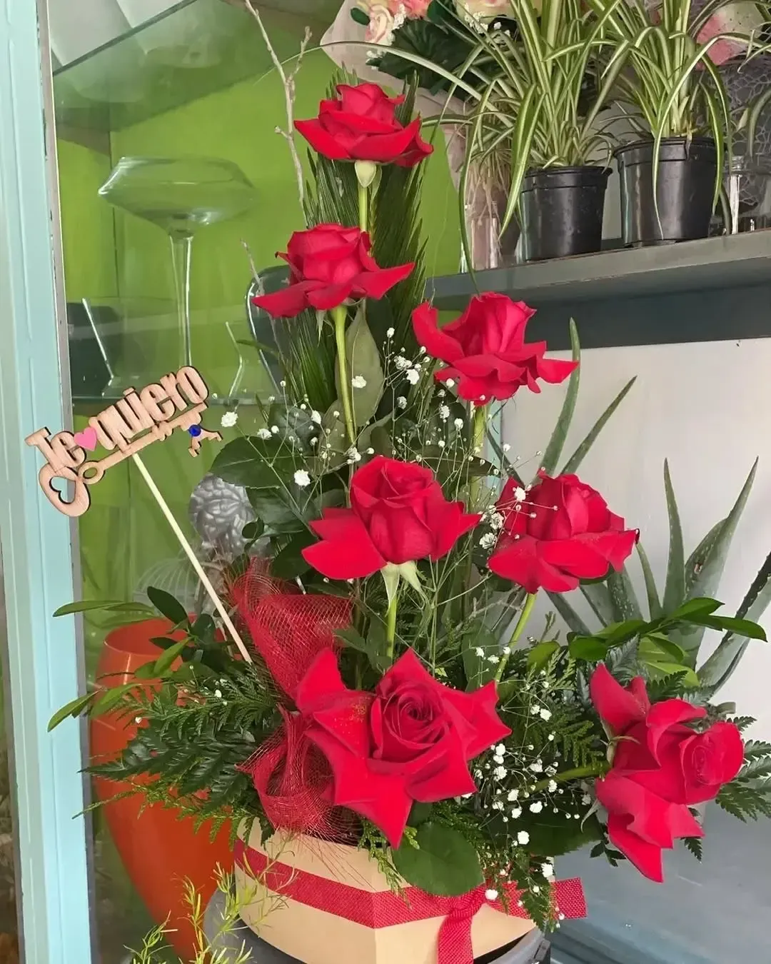 Un arreglo floral de rosas rojas y follaje en una caja de regalo, con un cartel que dice