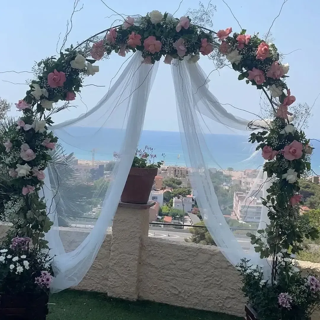 Un arco nupcial circular adornado con flores rosas y blancas y una tela blanca vaporosa con vistas a un paisaje