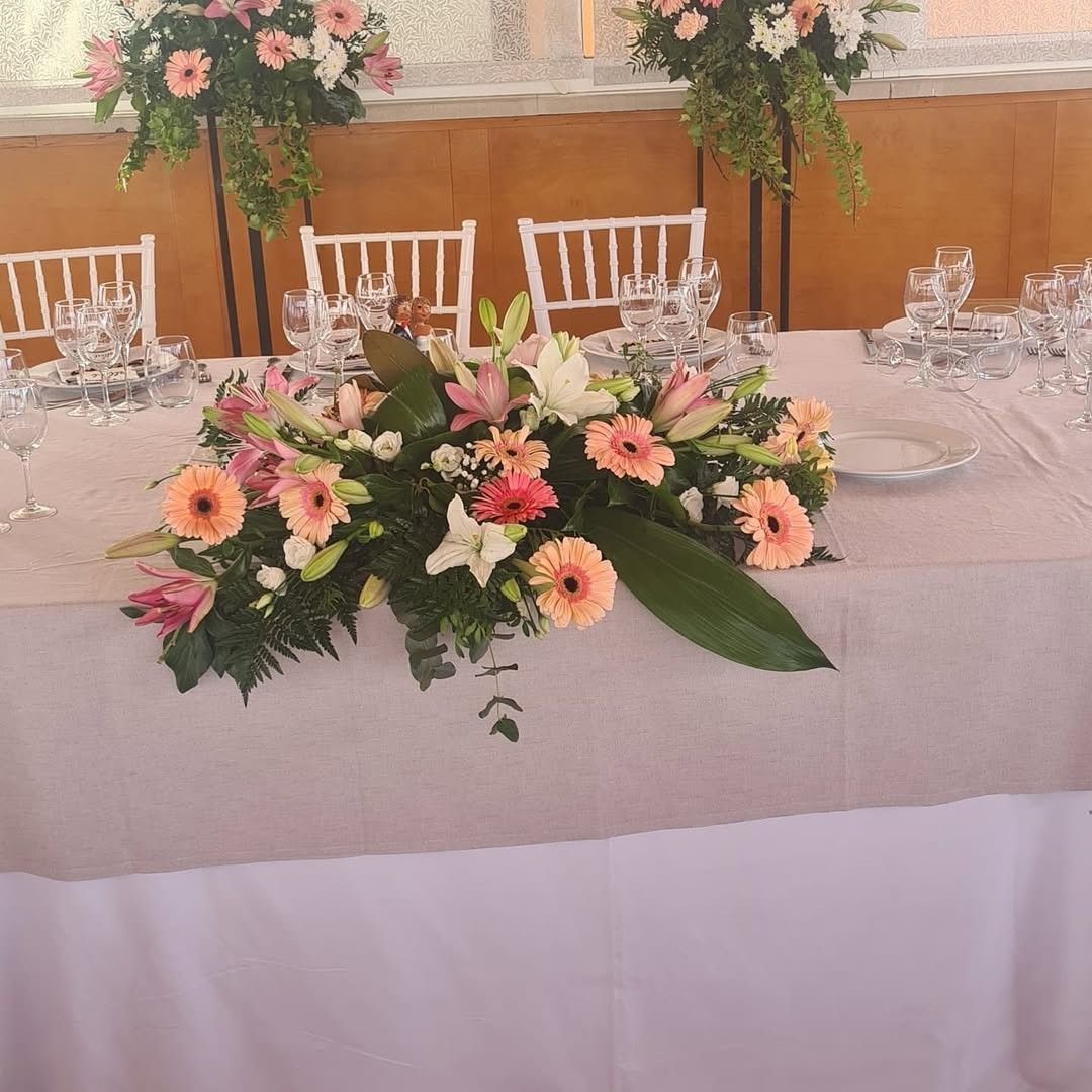 Una mesa formal para eventos con un mantel claro, dispuesta con cristalería y adornada