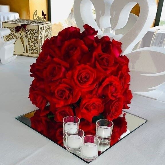 Un centro de mesa floral compuesto por vibrantes rosas rojas sobre una base cuadrada de espejo