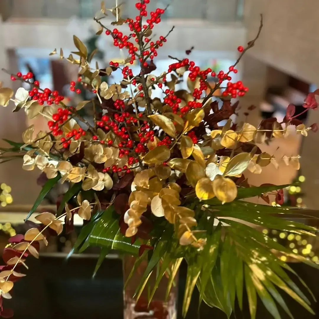 Un arreglo floral en un jarrón con eucalipto pintado de dorado, follaje rojo oscuro y bayas de color rojo