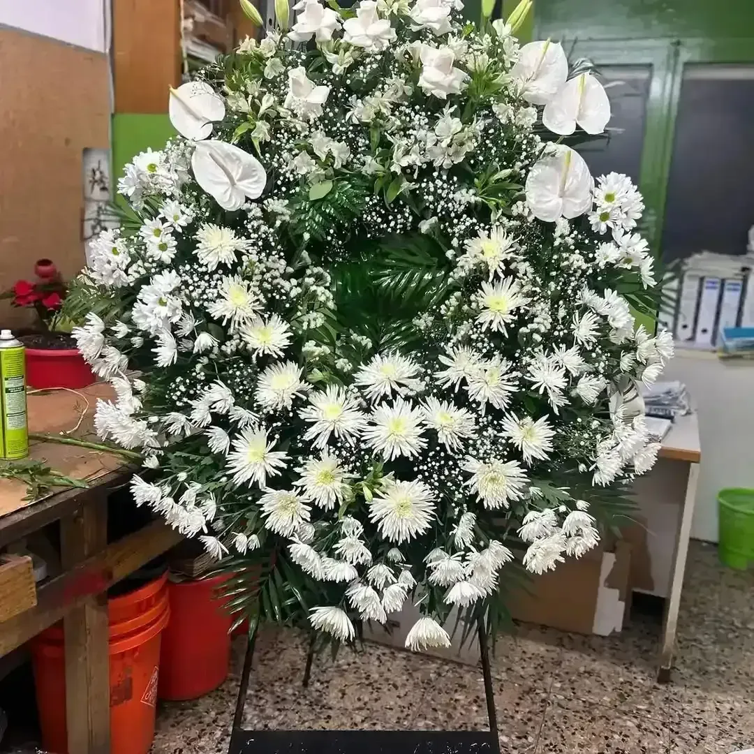 Una gran corona funeraria circular hecha de crisantemos blancos y anturios sobre un soporte de metal