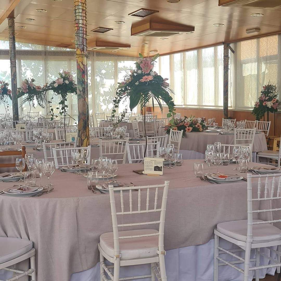 Un salón de banquetes preparado para un evento con mesas redondas, manteles de color rosa claro