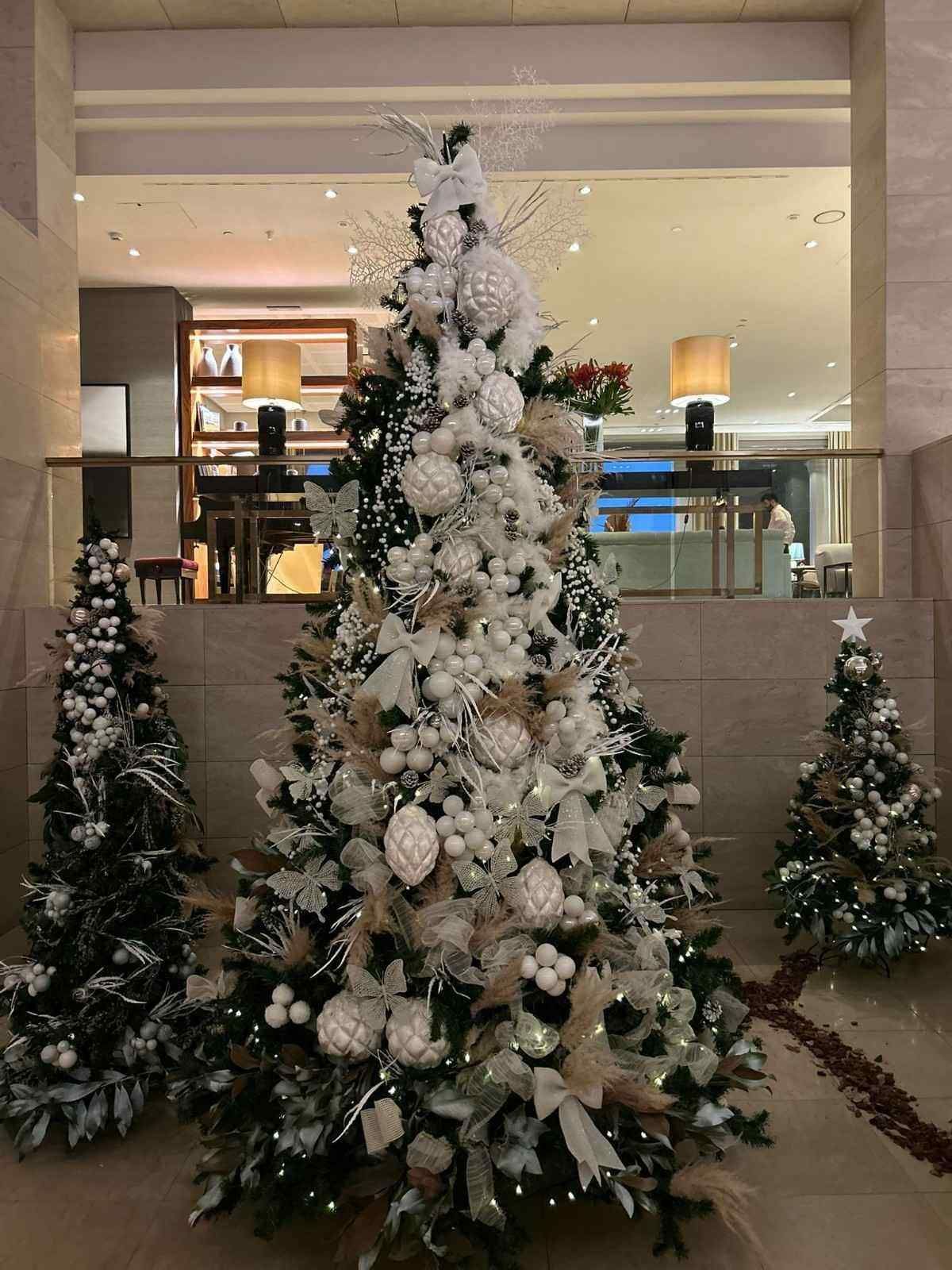 Un gran árbol de Navidad blanco y dorado, elaboradamente decorado, se encuentra en un vestíbulo entre dos árboles