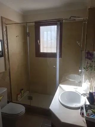 Un baño con inodoro, lavabo, ducha y ventana.