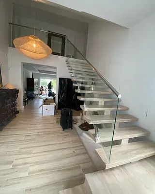 Una escalera blanca con barandilla de cristal en una sala de estar.