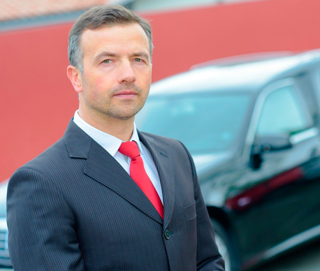 Un hombre con traje y corbata está parado frente a un automóvil.