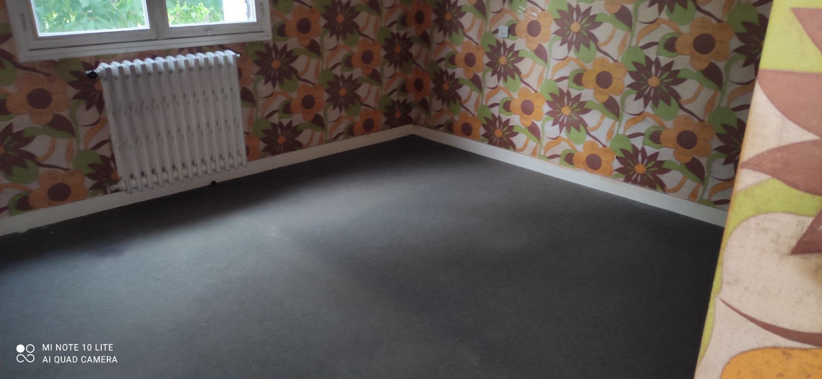 Chambre vide avec papier peint floral et sol en moquette noire et radiateur