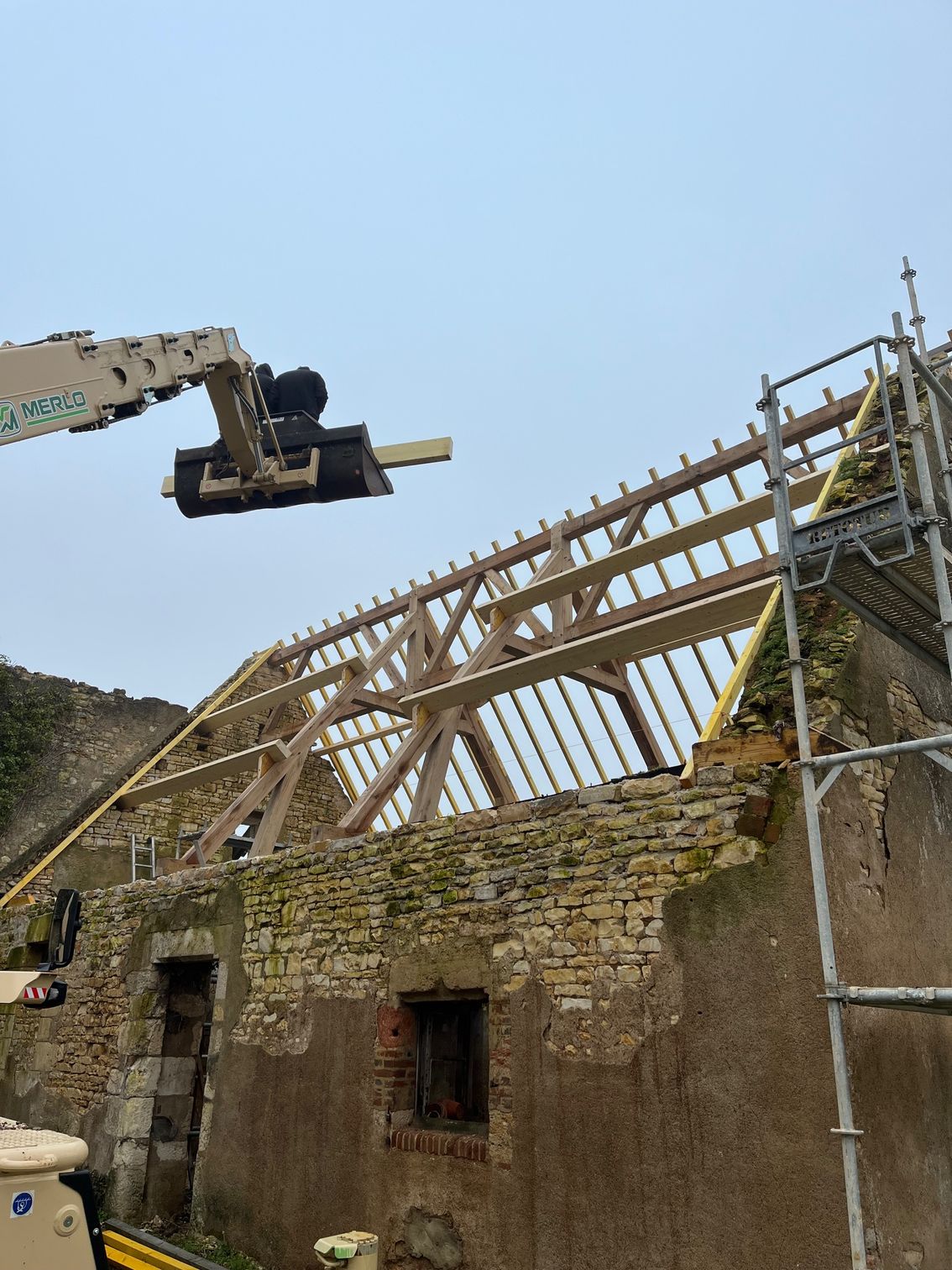 Utilisation d'une pelle pour disposer une poutre sur la charpente neuve d'une maison en rénovation
