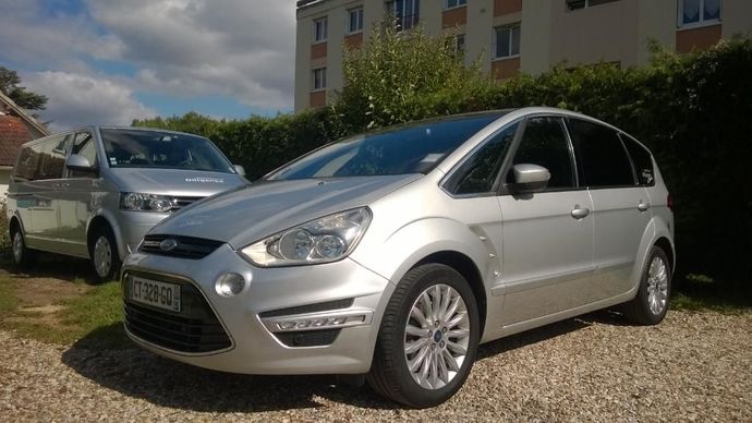 Un monospace gris garé devant une haie