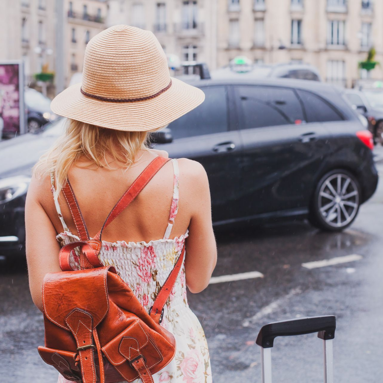 Une femme avec un chapeau et un sac à dos marche près d’une voiture