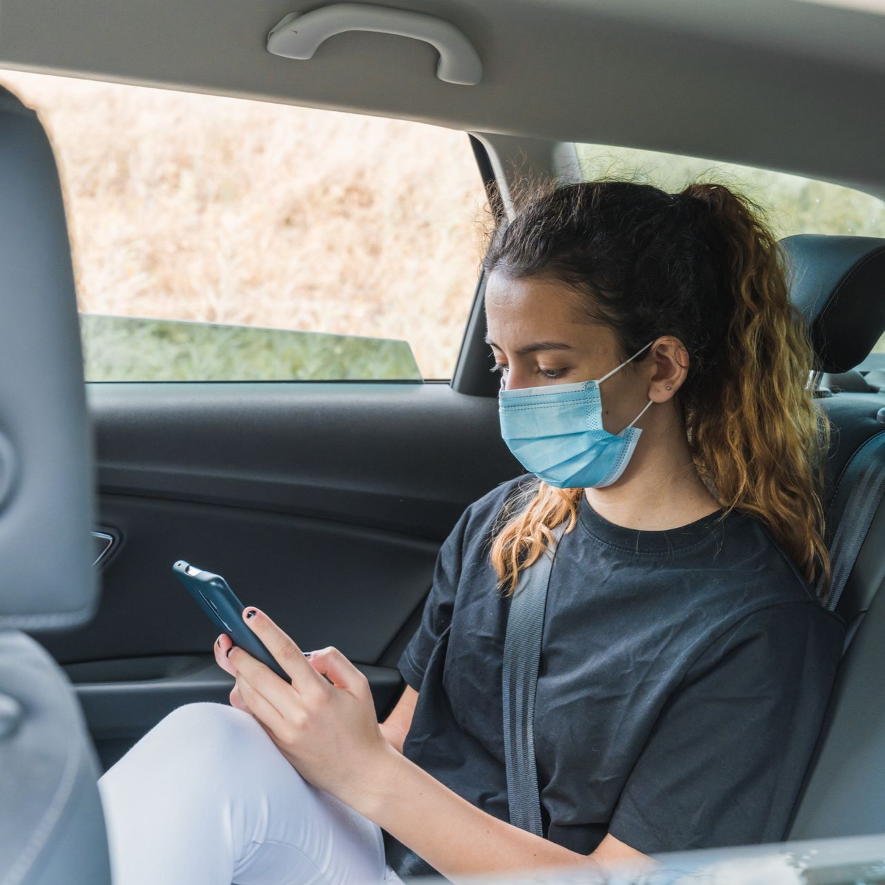 Une passagère masquée utilise son téléphone à l’arrière d’un taxi conventionné