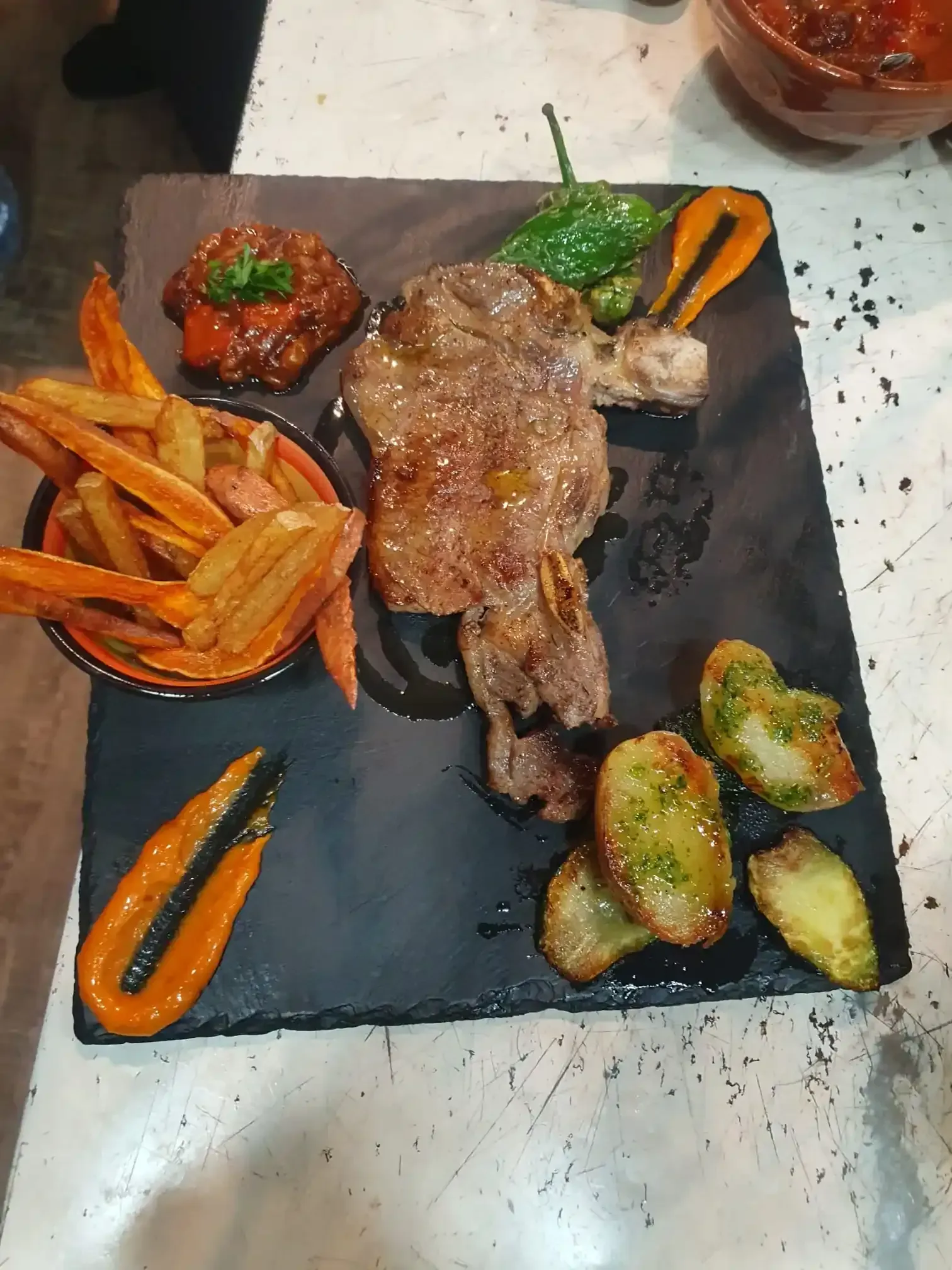 Filete a la parrilla con patatas fritas y verduras en un plato de pizarra negra, servido en una mesa.