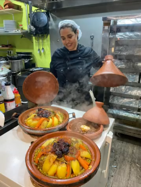 El vapor se eleva de dos tajines mientras un chef sirve la comida en una cocina.